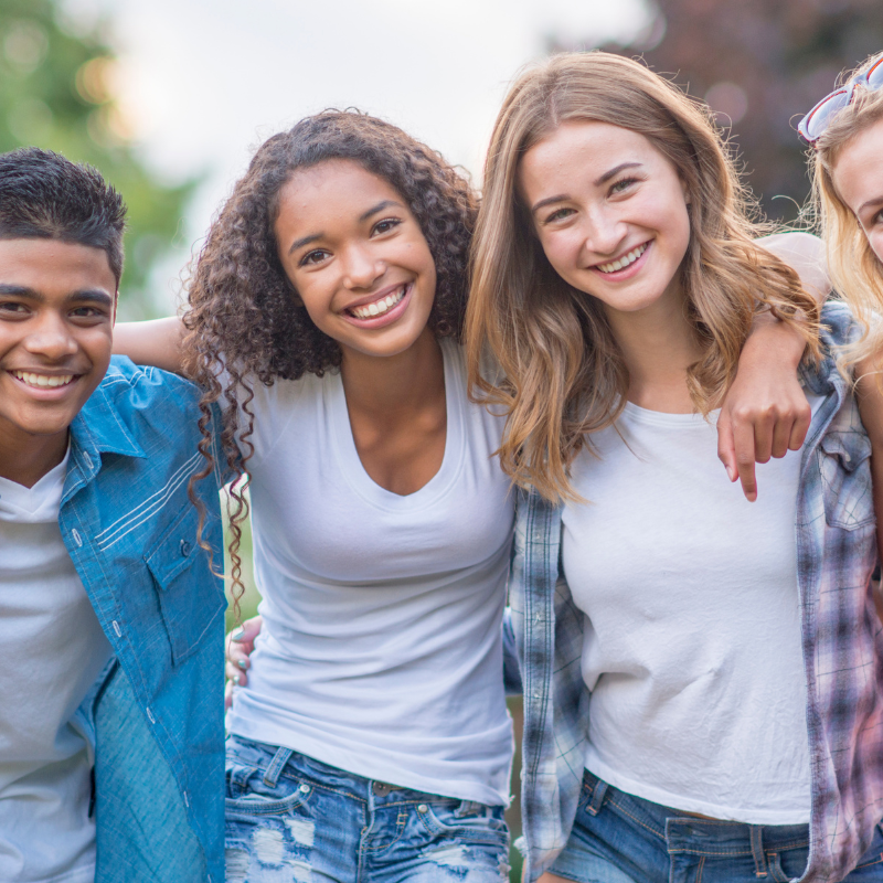 Teens standing arm in arm outside.