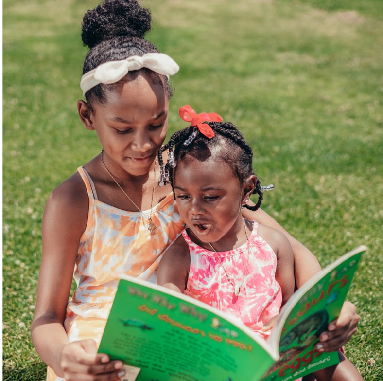 Two children reading a book together outside